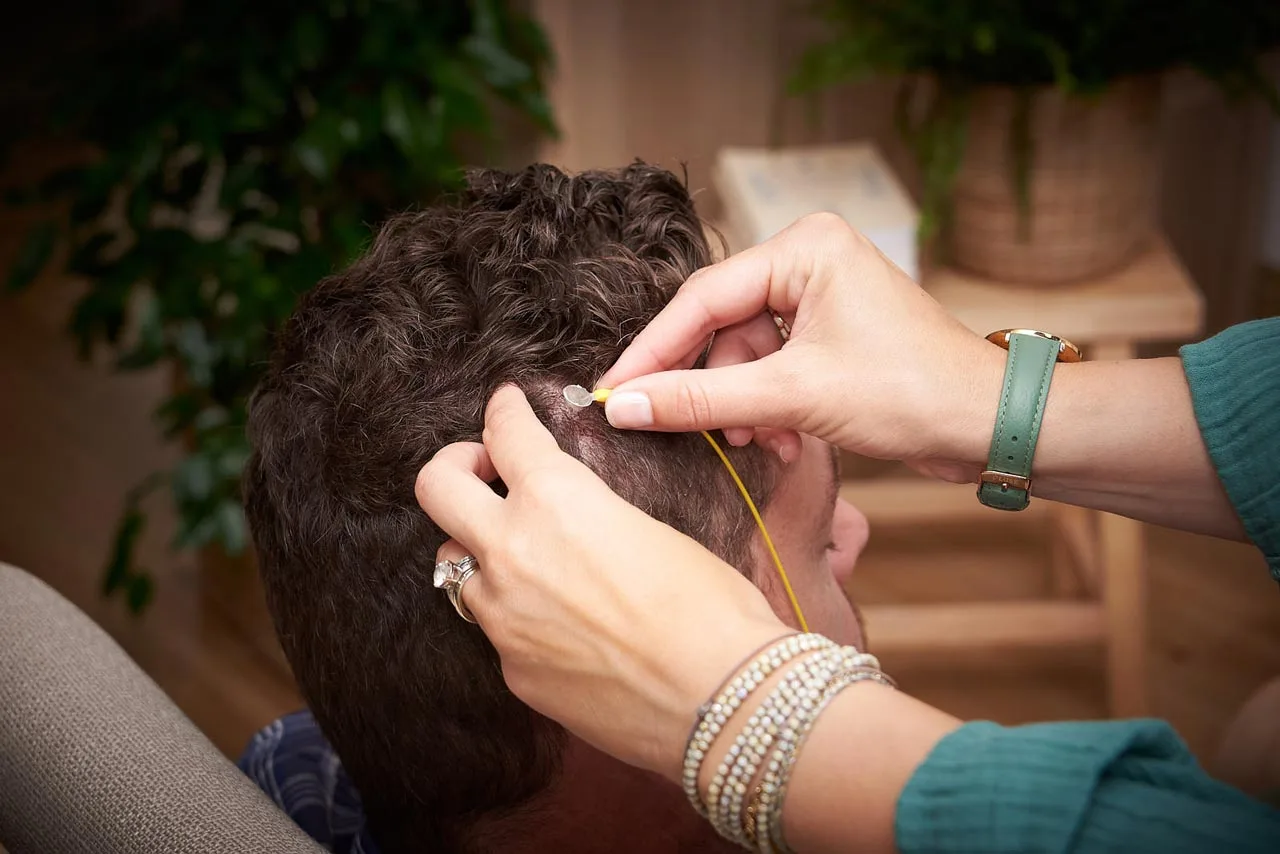 La praticienne pose un capteur de neurofeedback sur le cuir chevelu d'un client installé dans le fauteuil